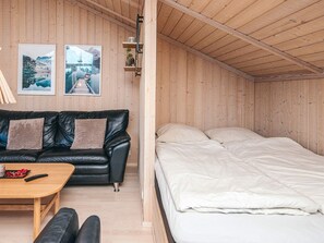 A cozy room with a black leather sofa, a wooden table, and a bed with white bedding. - 4 Star Holiday Home in Ebeltoft (Ebeltoft)
