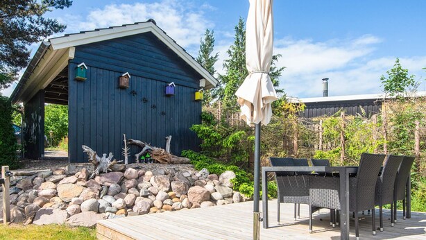 A wooden deck with a table and chairs, a blue building with birdhouses, and a stone wall. - 4 Star Holiday Home in Ebeltoft (Ebeltoft)