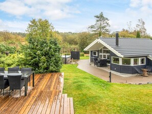 Ein modernes Haus mit Terrasse, überdachter Sitzgelegenheit und einem großen Baum.