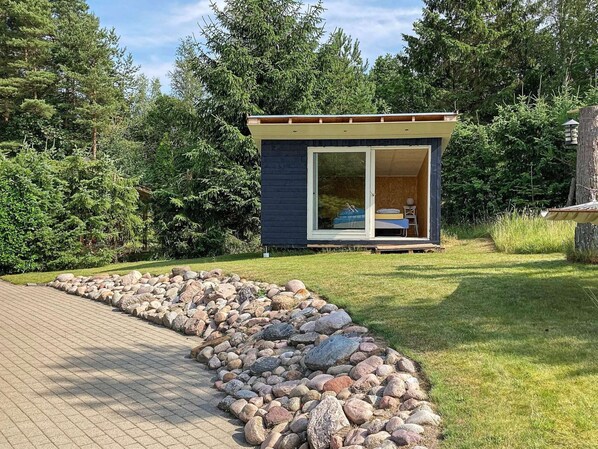 Une petite cabane avec une porte-fenêtre coulissante, un lit et une chaise à l’extérieur.