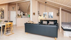 A cozy loft-style room with a high ceiling, wooden walls, a dining area with a table and chairs, a sofa, and a bed. - 4 Star Holiday Home in Ebeltoft (Ebeltoft)
