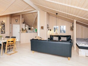 A cozy loft-style room with a high ceiling, wooden walls, a dining area with a table and chairs, a sofa, and a bed. - 4 Star Holiday Home in Ebeltoft (Ebeltoft)