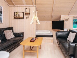 A cozy living room with a wooden ceiling, a black leather sofa, a wooden coffee table, and a TV mounted on the wall. - 4 Star Holiday Home in Ebeltoft (Ebeltoft)