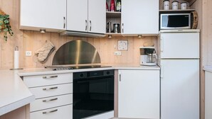 A modern kitchen with white cabinetry, stainless steel appliances, and a microwave on top of a refrigerator. - 4 Star Holiday Home in Ebeltoft (Ebeltoft)
