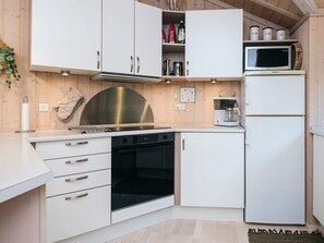 A modern kitchen with white cabinetry, stainless steel appliances, and a microwave on top of a refrigerator. - 4 Star Holiday Home in Ebeltoft (Ebeltoft)