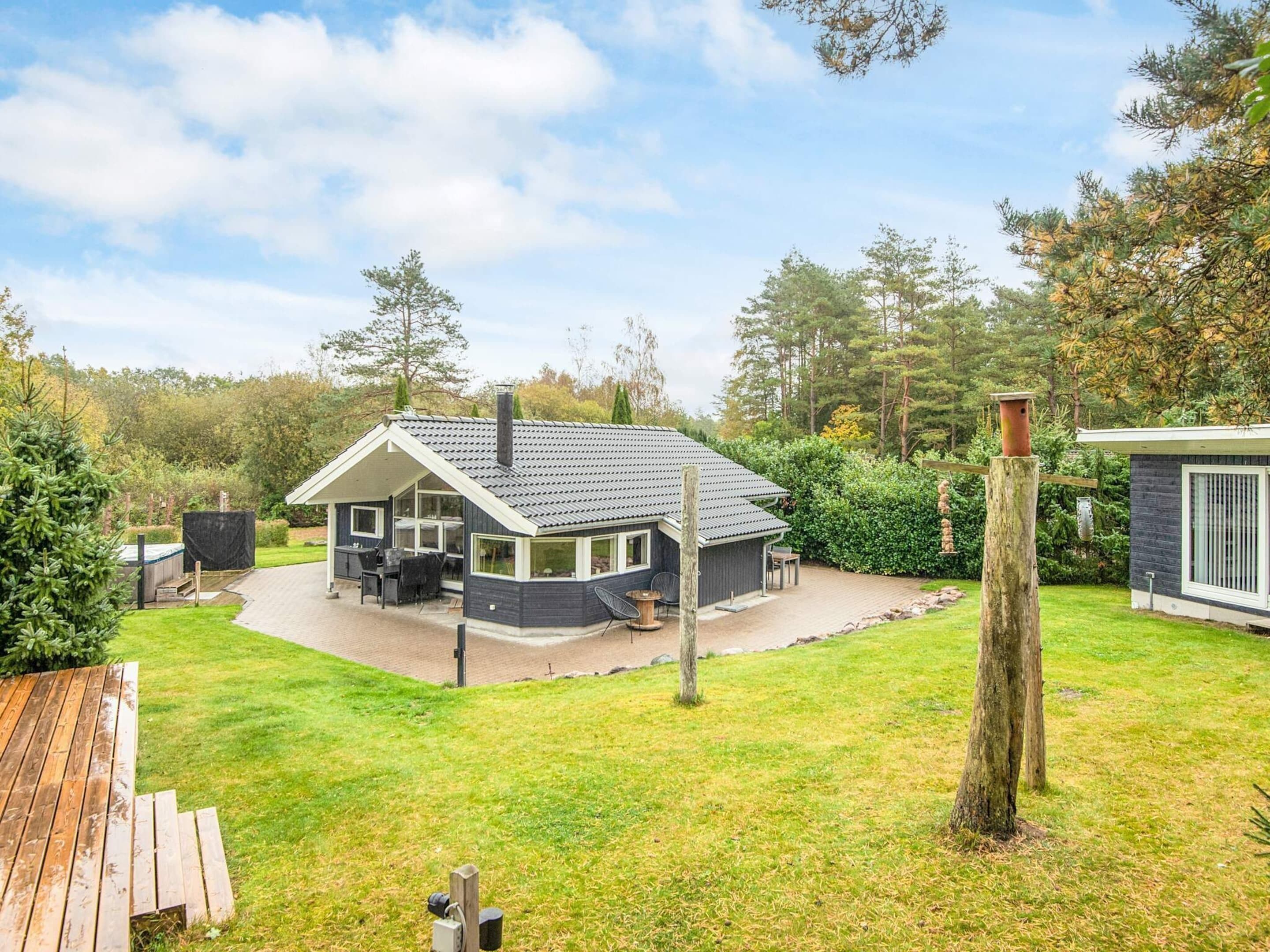 Ein Haus mit überdachter Terrasse, Schornstein und umzäunter Garten.