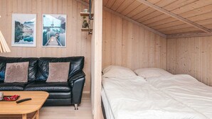 A room with a black leather sofa, a wooden coffee table, a bed with white bedding, and two framed pictures on the wall. - 4 Star Holiday Home in Ebeltoft (Ebeltoft)