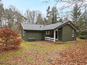 A small, single-story cabin with a porch, surrounded by trees and fallen leaves.