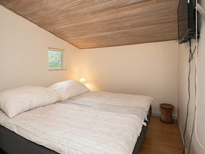 A bedroom with a wooden ceiling, a bed with white bedding, a bedside lamp, a small window, and a wall-mounted TV. - 5 Person Holiday Home in Thyholm (Thyholm)
