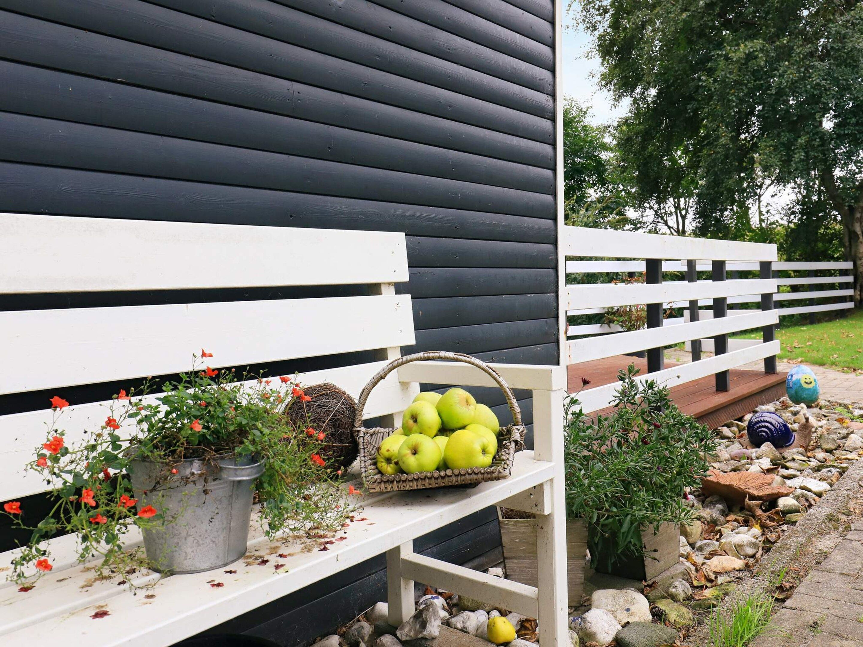 A bench with a basket of green apples and a potted plant with red flowers.