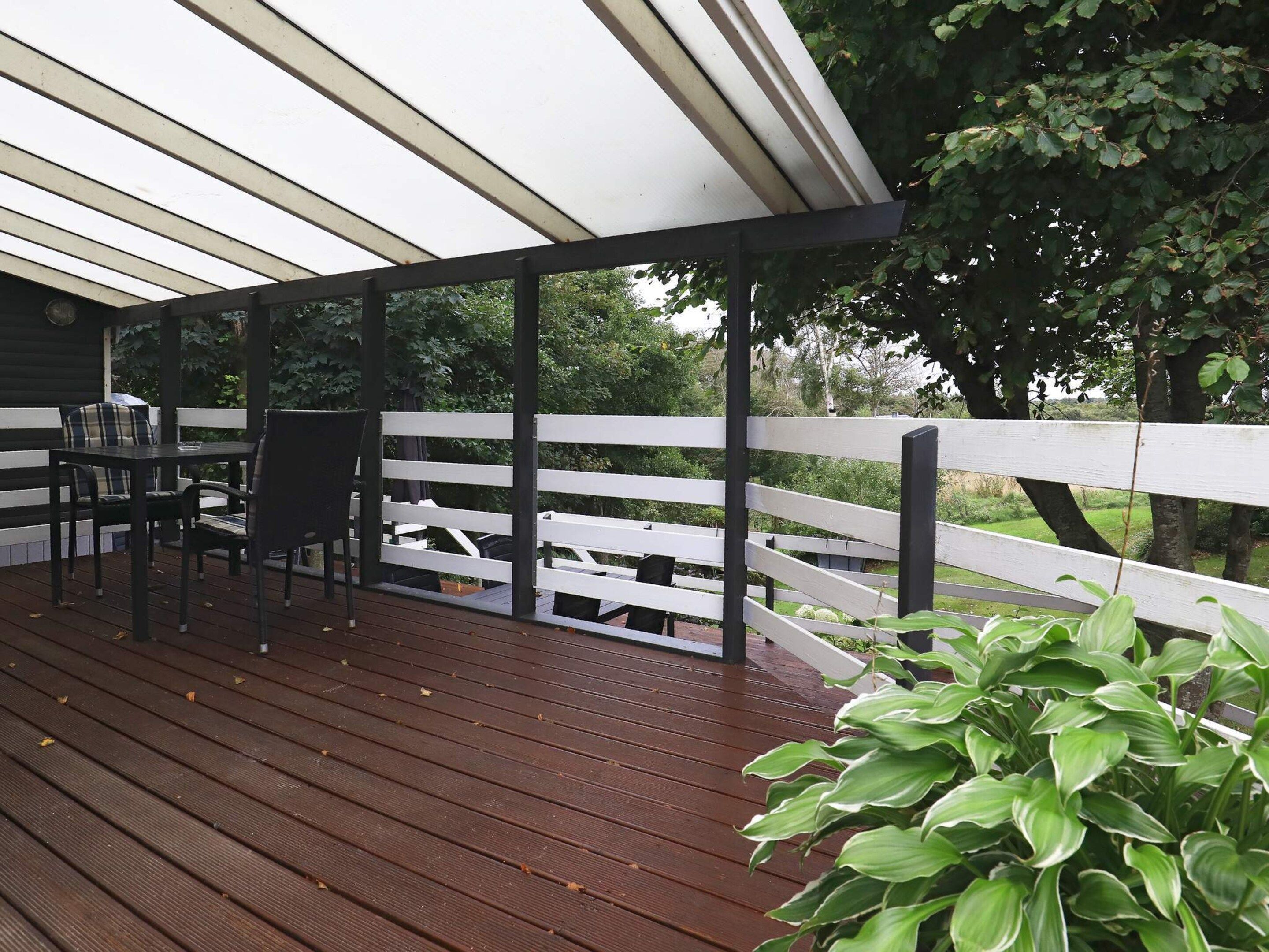 A covered outdoor deck with a wooden floor, a table with chairs, and a white railing.