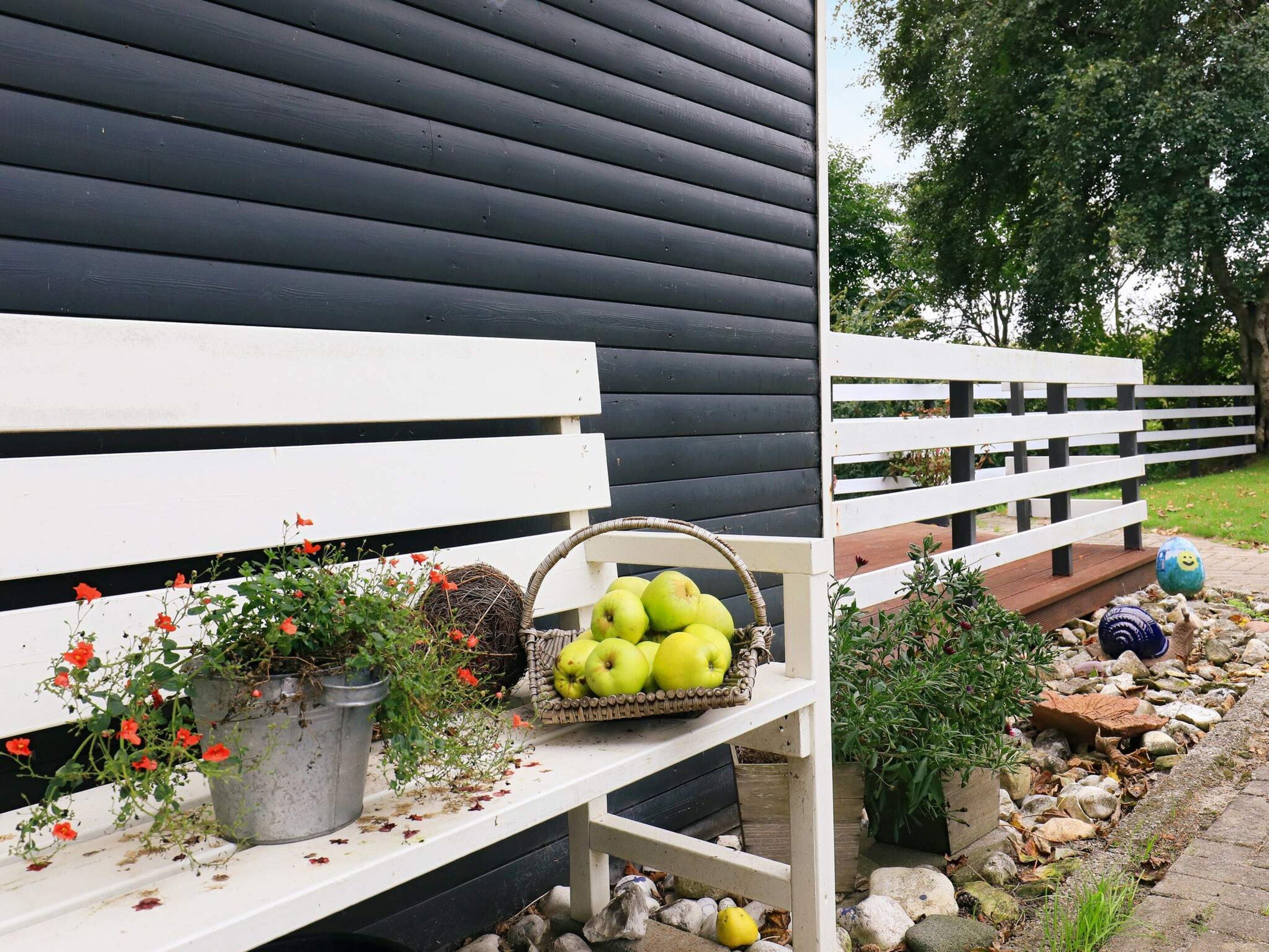 A bench with a basket of green apples and a potted plant with red flowers.