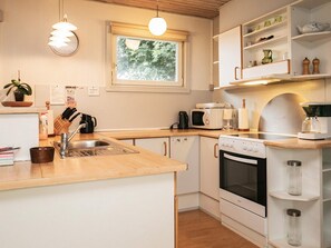 A compact kitchen with a sink, stove, microwave, and a window with a view of trees.