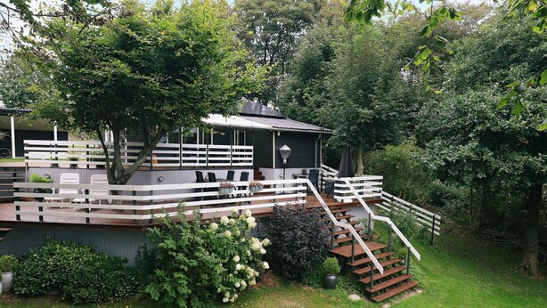 A residential property with a wooden deck, outdoor seating, and a staircase leading to a covered area. - 5 Person Holiday Home in Thyholm (Thyholm)