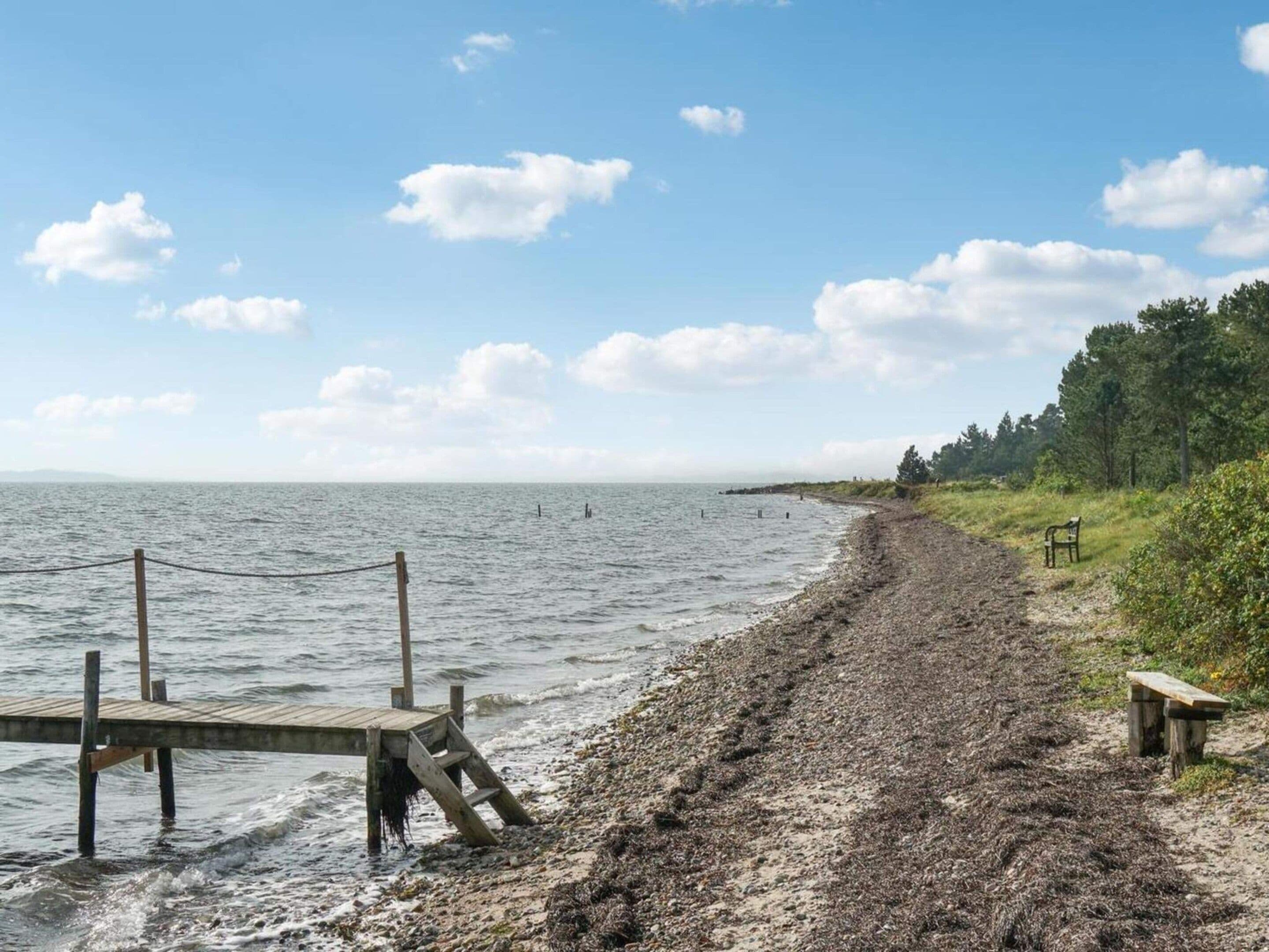 Ein Strand mit einer Holzstege, einer Bank und einem Weg zum Wasser.