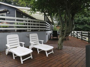 A wooden deck with two white lounge chairs, a table, and a tree. - 5 Person Holiday Home in Thyholm (Thyholm)