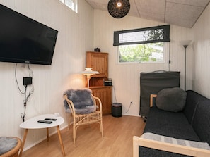 A room with a flat-screen TV, a sofa, a chair, a small table, and a window with a view of greenery. - 5 Person Holiday Home in Thyholm (Thyholm)