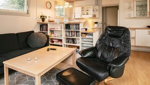 A living room with a black leather chair, a wooden table, a bookshelf, and a kitchen area with cabinets. - 5 Person Holiday Home in Thyholm (Thyholm)