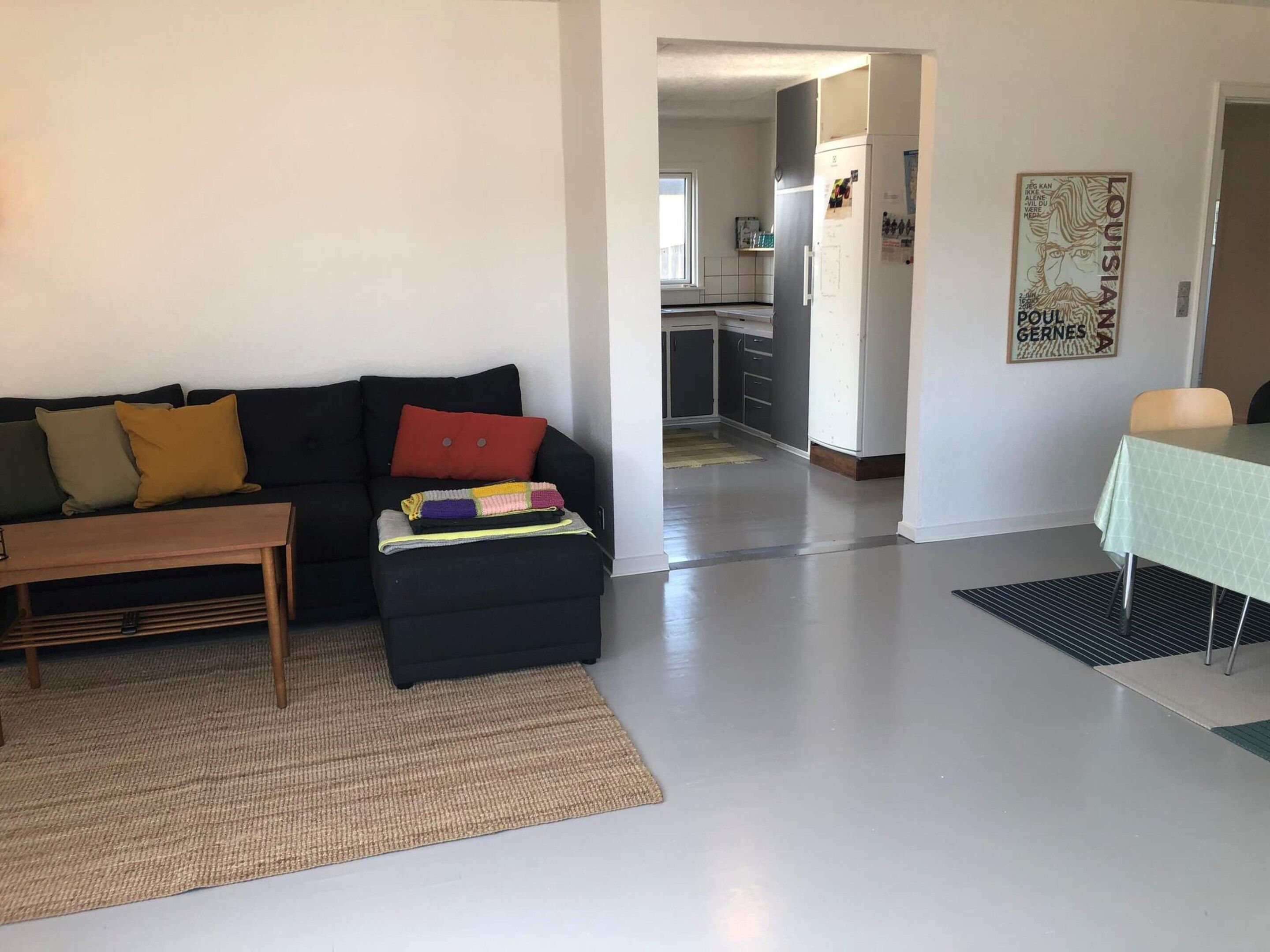 Un salon avec un canapé, une petite table, une cuisine à l’arrière-plan et une affiche accrochée au mur.
