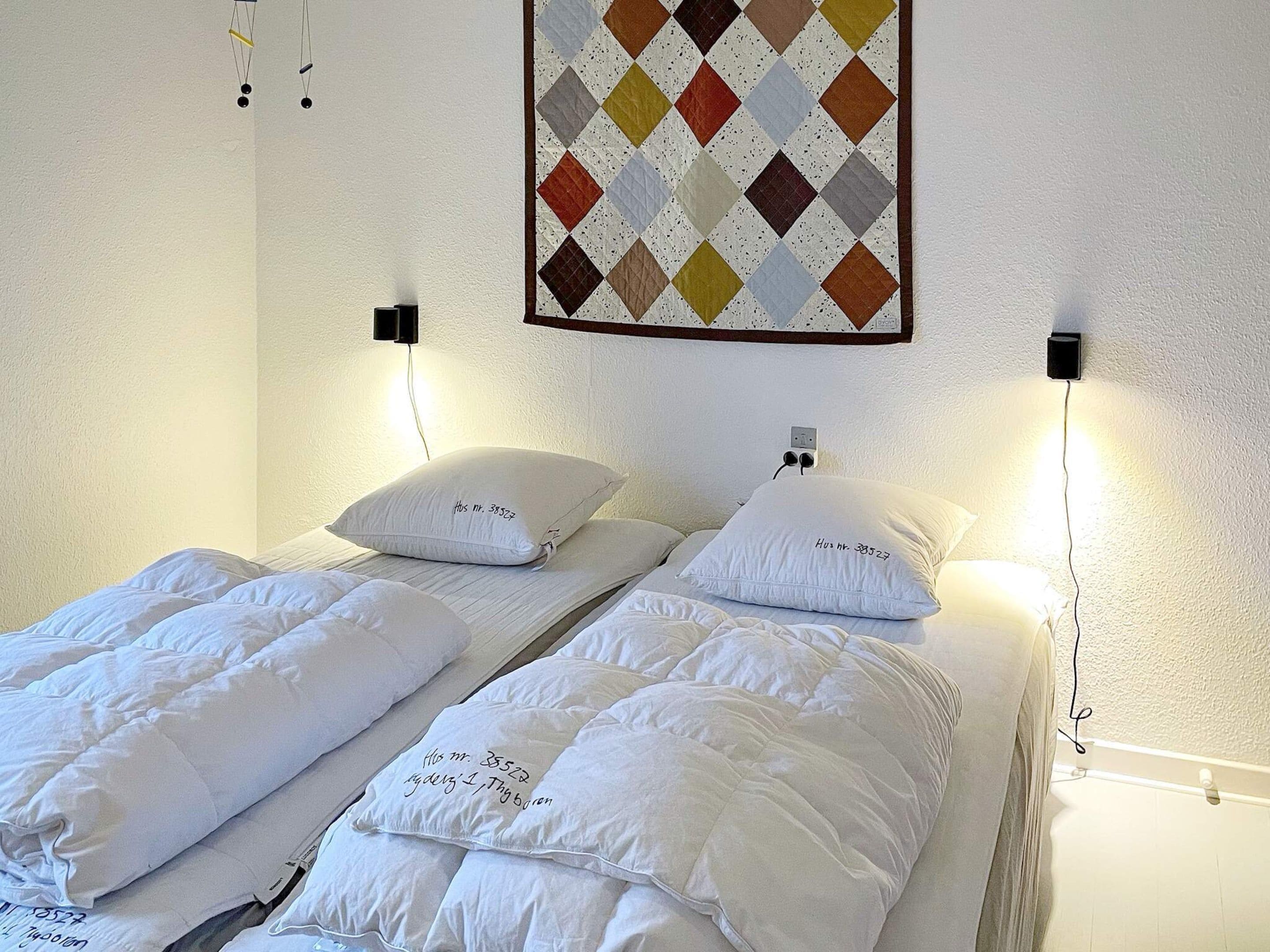 A hotel room with two beds, each with white bedding and pillows, a quilted blanket, and a wall-mounted quilt with a diamond pattern.