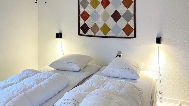 A hotel room with two beds, each with white bedding and pillows, a quilted blanket, and a wall-mounted quilt with a diamond pattern. - 4 Star Holiday Home in Thyboron (Thyborøn)