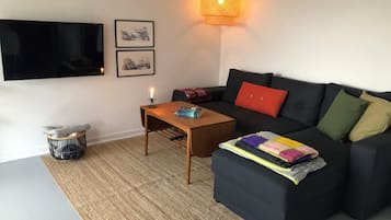 A living room with a sofa, a coffee table, a TV mounted on the wall, and a lamp.