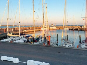 Un puerto deportivo con varios veleros amarrados, un muelle de madera y un cielo despejado.