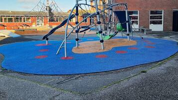 A playground with a climbing structure and slides, surrounded by a blue rubberized surface with red circles.