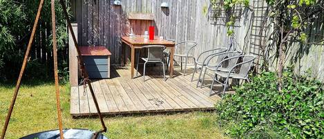 A wooden deck with a table and chairs, a hanging light fixture, and a wheelbarrow with firewood.