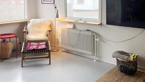 A living room with a chair, a small table, a radiator, a TV, and a window with a view of a house. - 4 Star Holiday Home in Thyboron (Thyborøn)