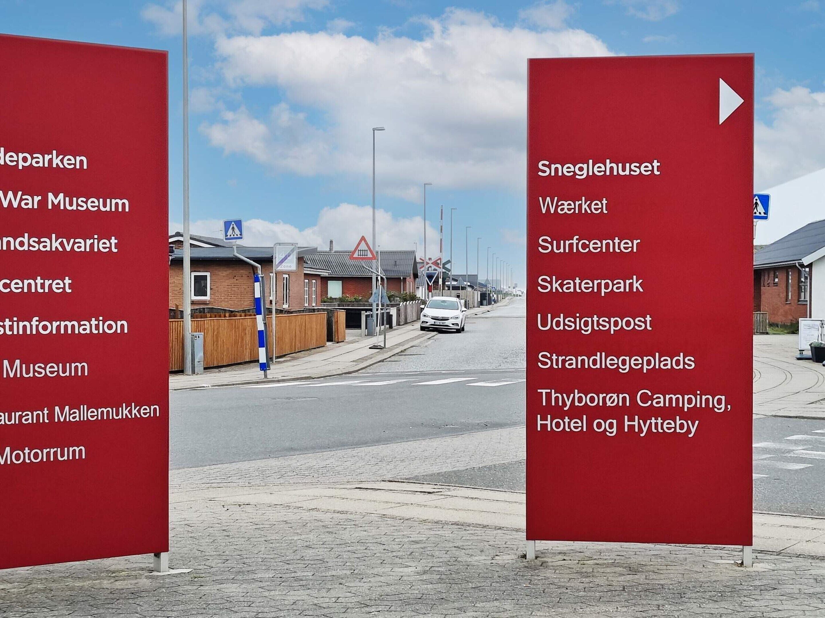 A street view with red directional signs listing various attractions and facilities.