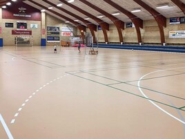 Una cancha de deportes interior con un aro de baloncesto, una red de voleibol y una red de tenis.
