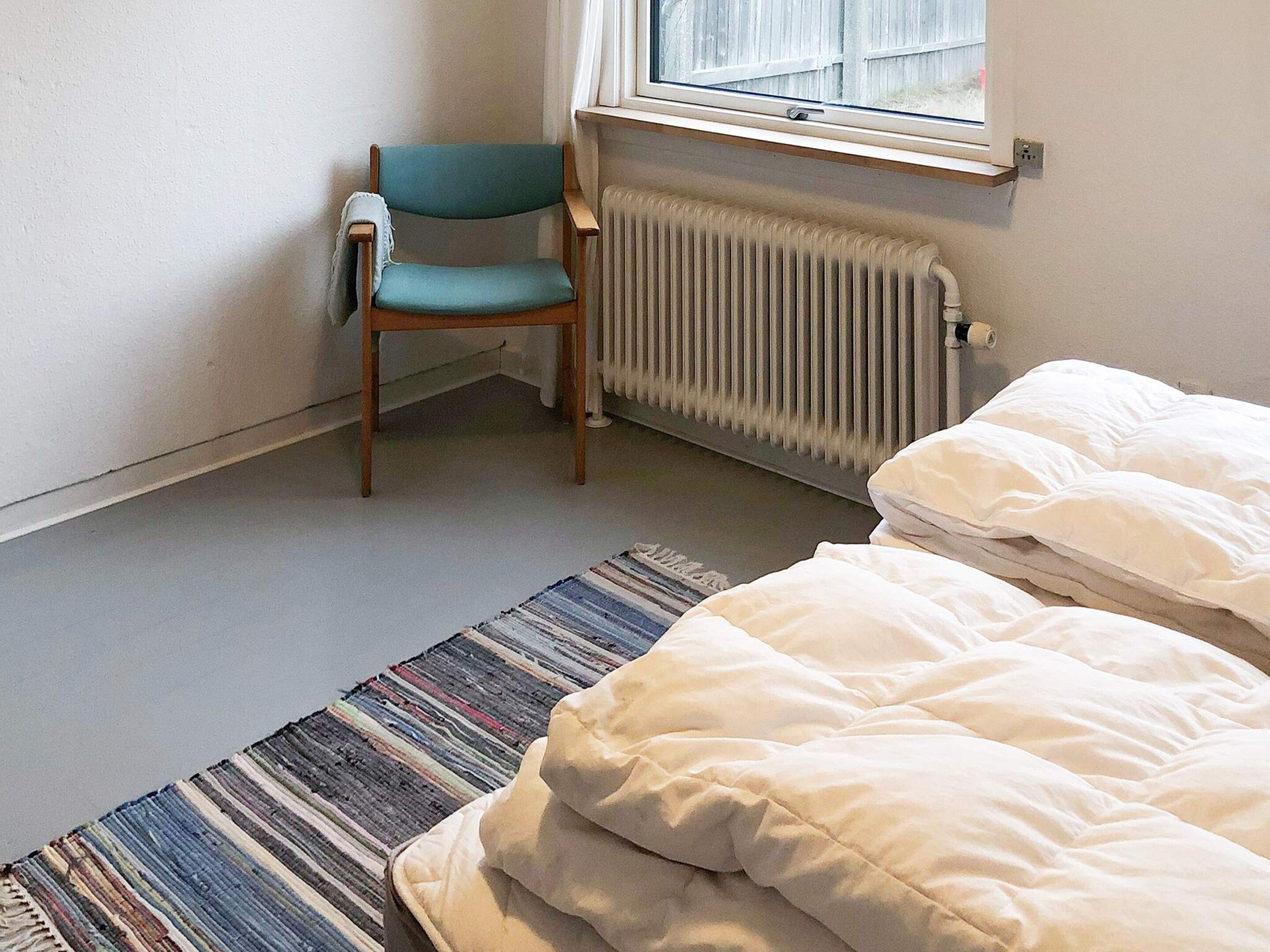 Ein Zimmer mit einem Einzelbett, einem Sessel, einer Heizung und einem Fenster.