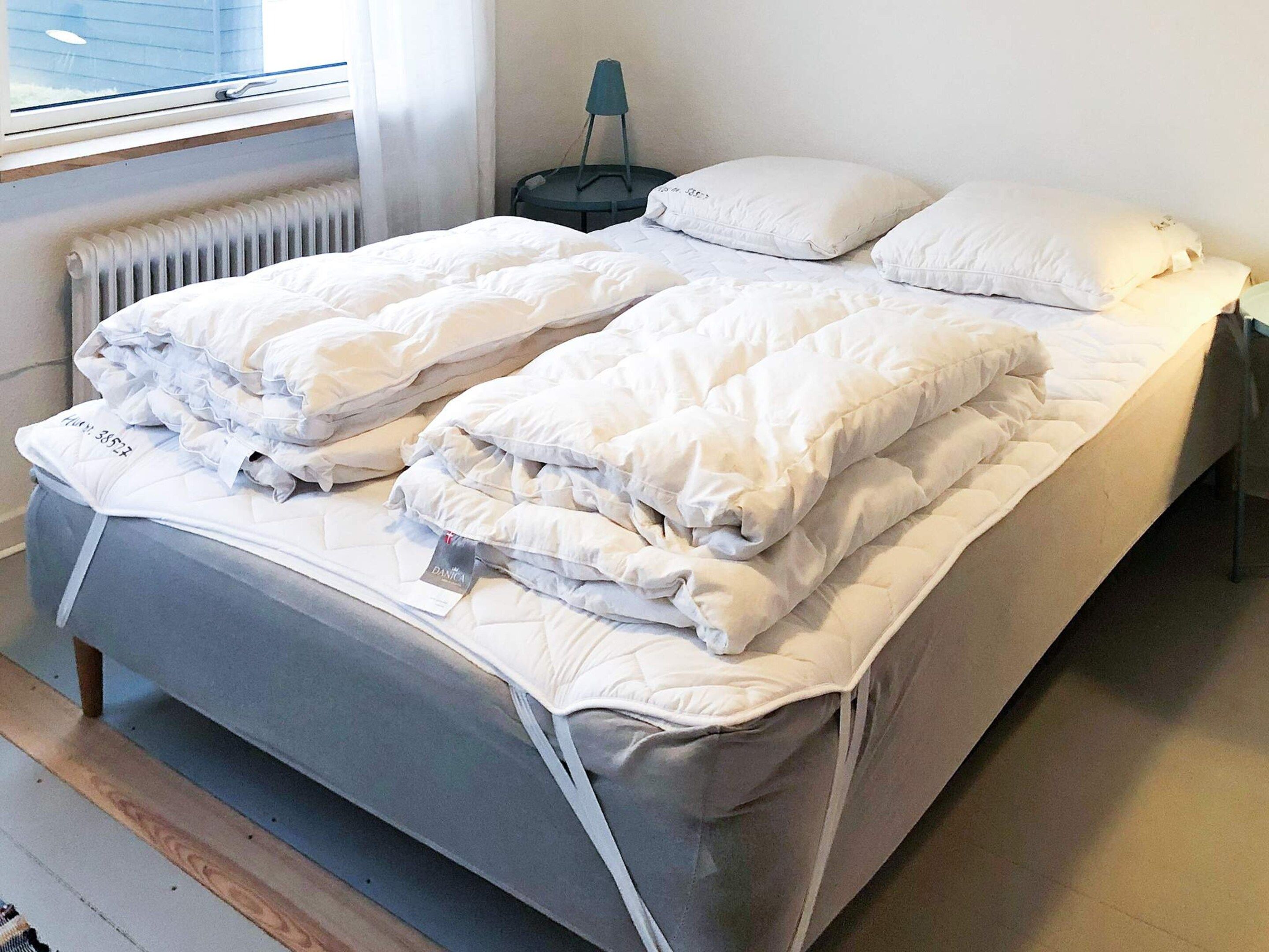A double bed with white bedding, a bedside table with a lamp, and a window with blinds.