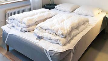 A double bed with white bedding, a bedside table with a lamp, and a window with blinds.