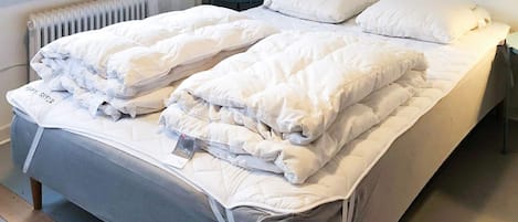 Ein Doppelbett mit weißer Bettwäsche, ein Nachttisch mit Lampe und ein Fenster mit Jalousien.