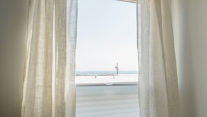 Une vue à travers des rideaux transparents donnant sur une plage avec un poste de surveillance pour les sauveteurs.