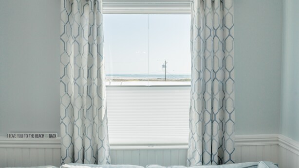 Une chambre avec vue sur la plage, un lit et une fenêtre avec des rideaux.