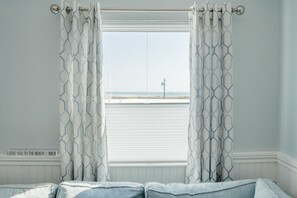 Ein Schlafzimmer mit Blick auf den Strand, ein Bett und ein Fenster mit Vorhängen.