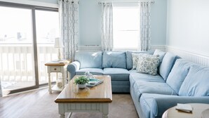 Une pièce avec un canapé bleu clair, une table basse en bois ornée d ’une plante, et une vue sur l’extérieur grâce à une grande fenêtre.