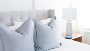 Une chambre à coucher avec un lit blanc, des oreillers bleu clair, un lustre noir et une table de chevet blanche avec une lampe.