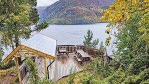 Eine Holzterrasse mit Picknicktischen mit Blick auf einen See, umgeben von Bäumen und Hügeln.