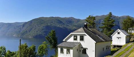 A white house with a sloped roof, a small attached garage, and a view of a lake and mountains in the background.
