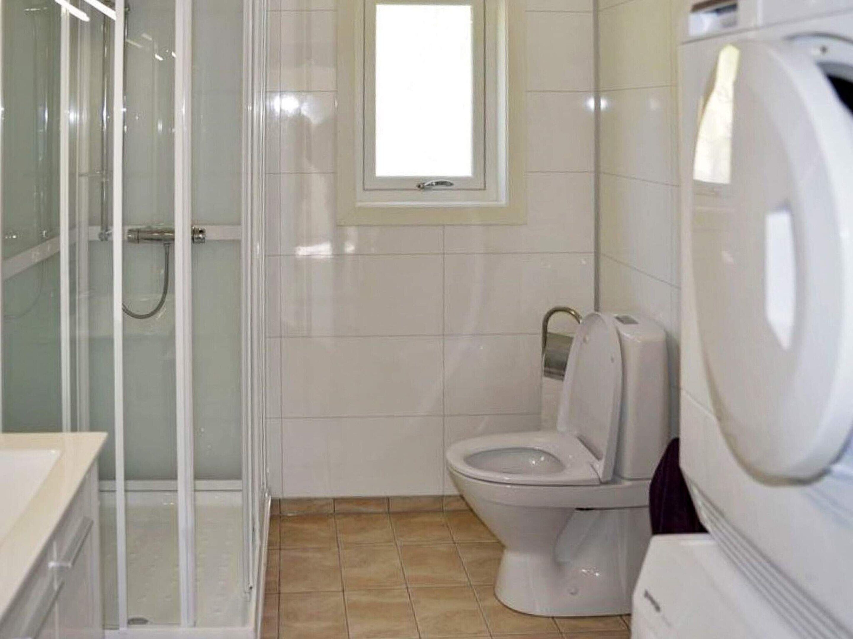 A bathroom with a glass shower enclosure, a toilet, and a washing machine.