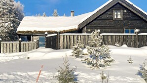 Una cabaña de madera con techo cubierto de nieve y una valla de madera.