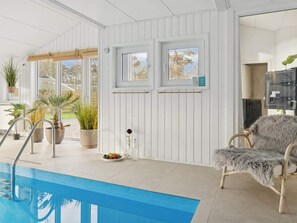 A pool area with a blue pool, white walls, and a wicker chair. - 5 Star Holiday Home in Nexo (Nexø)