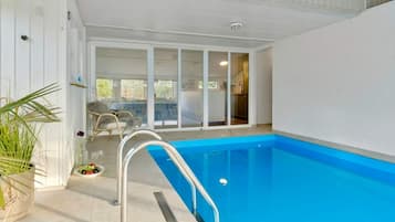 An indoor swimming pool with a clear view of the adjacent room through glass doors.