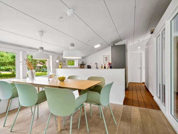 A modern kitchen with white cabinetry, a wooden countertop, and a dining area with a wooden table and green chairs. - 5 Star Holiday Home in Nexo (Nexø)