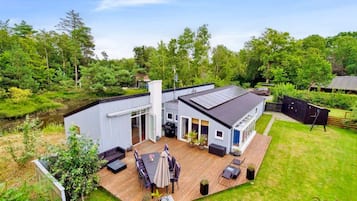 A modern house with a deck, a barbecue area, and a large window overlooking a lush garden.