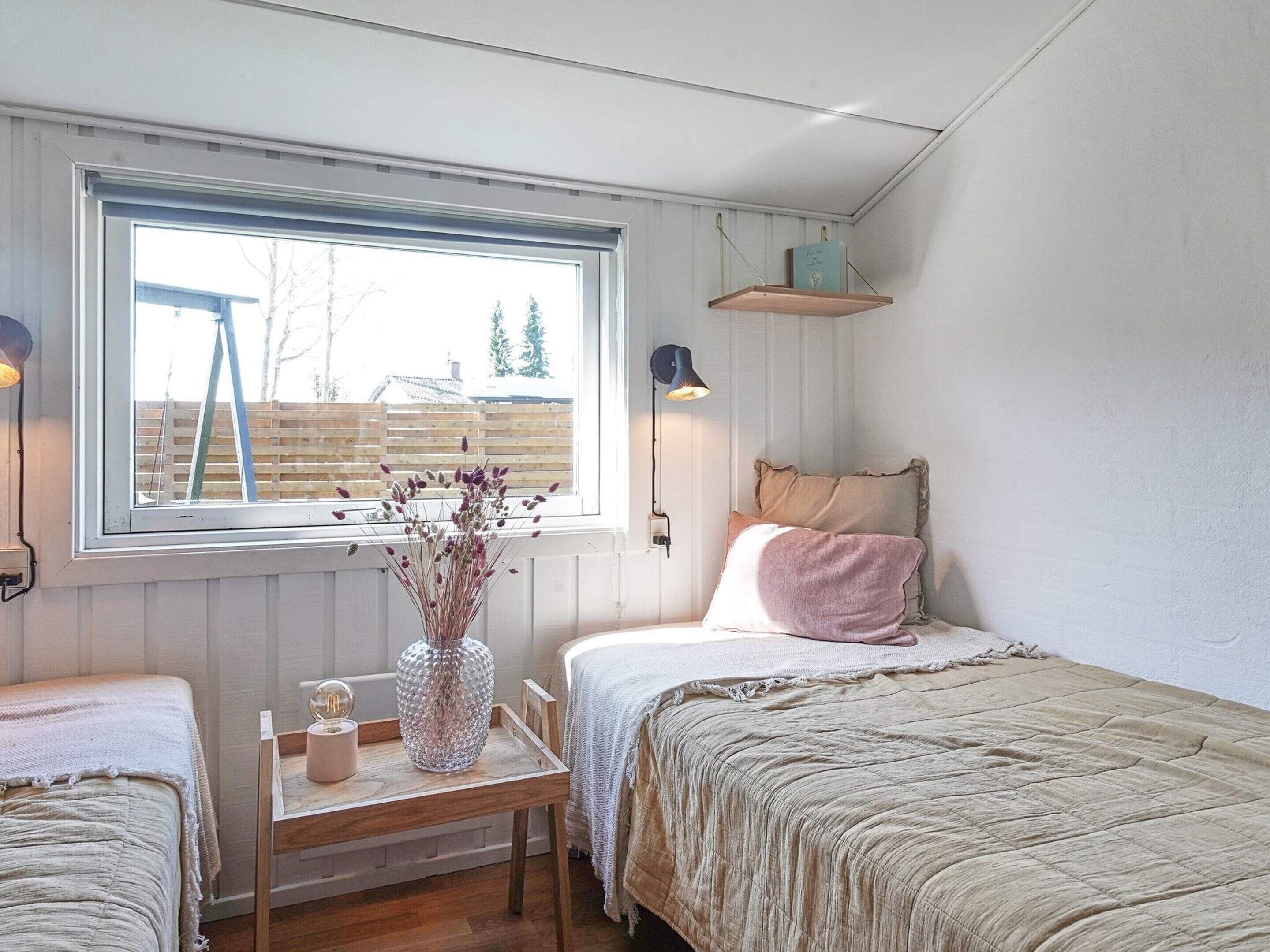 Ein Schlafzimmer mit zwei Betten, einem Fenster mit Aussicht, einem Nachttisch mit einer Vase und einer Lampe.